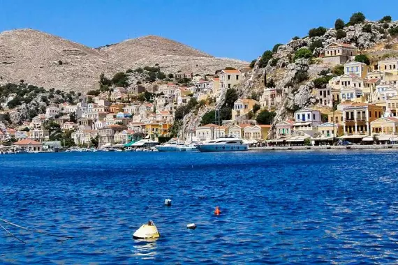 Île de Tilos, dans le Dodécanèse : panorama, depuis la mer, avec des bateaux et une ville en arrière-plan